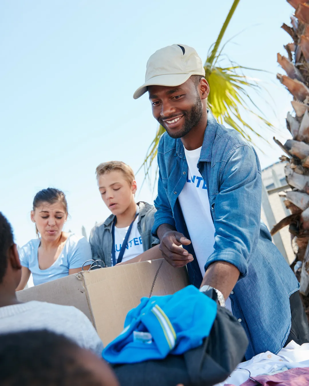 Volunteers smiling together outdoors as they sort donated goods on a sunny afternoon
