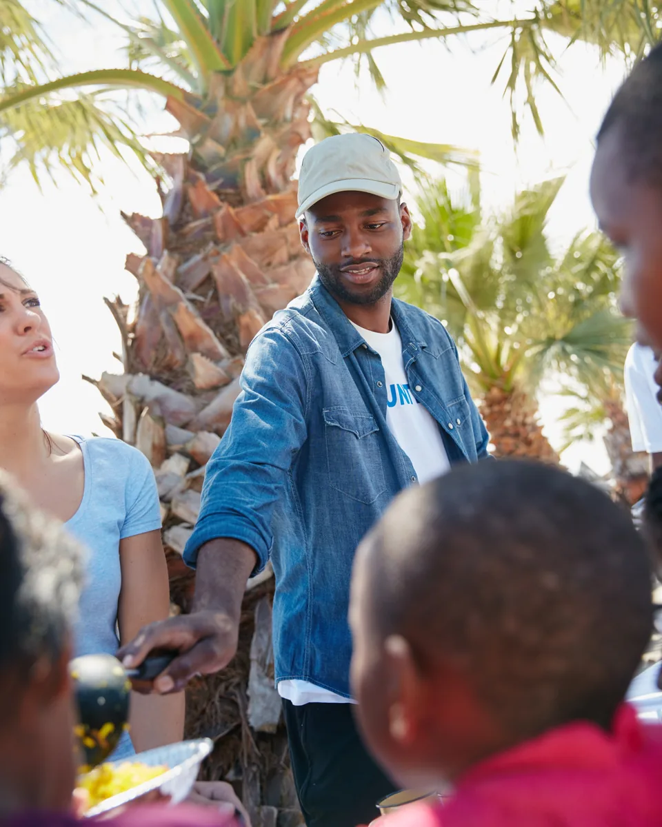 A volunteer handing a plate of food to children at an outdoor distribution